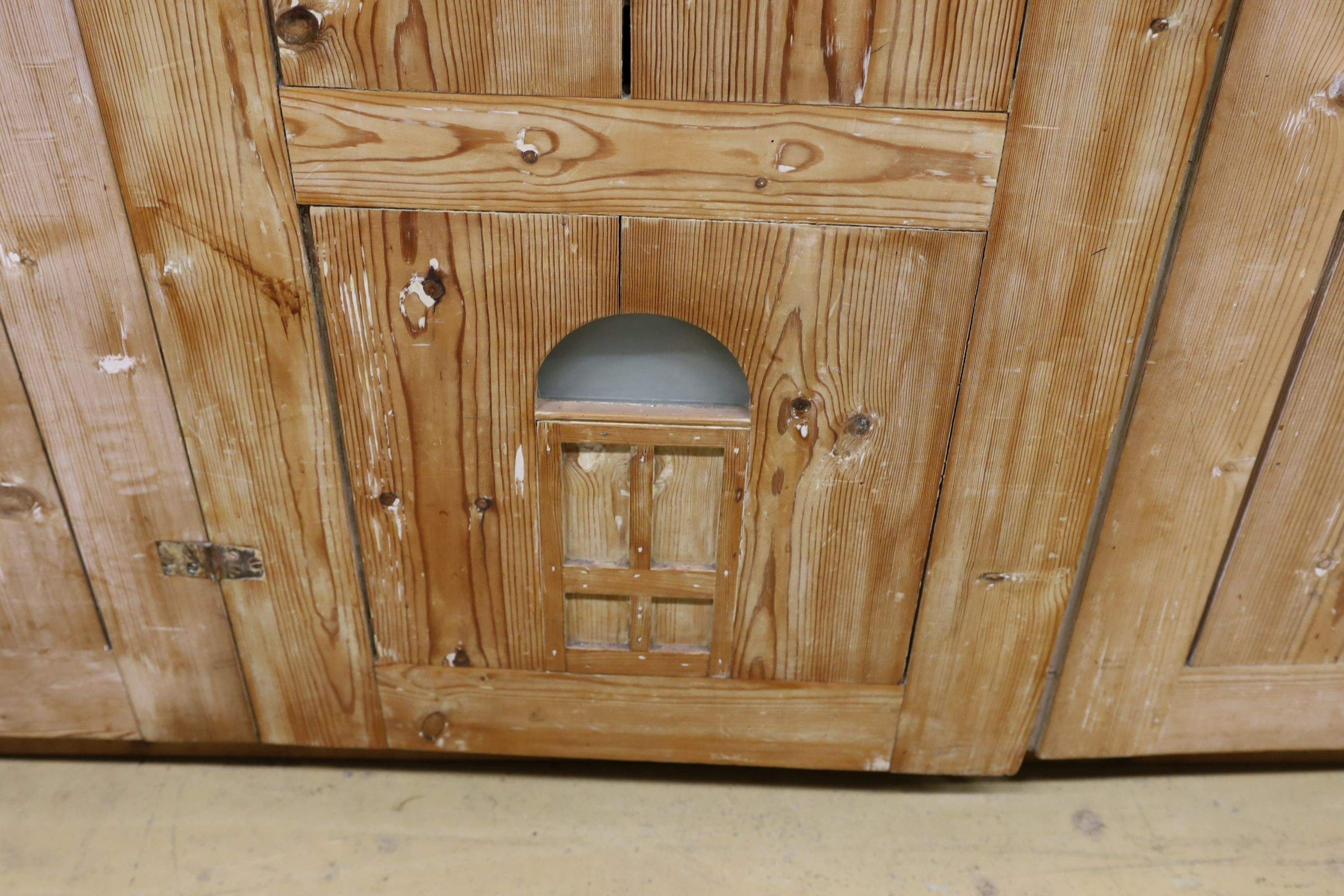 A 19th century stripped pine hall cupboard modelled as a dolls house the two door nine window facade enclosing a compartmented interior, width 182cm, depth 46cm, height 192cm